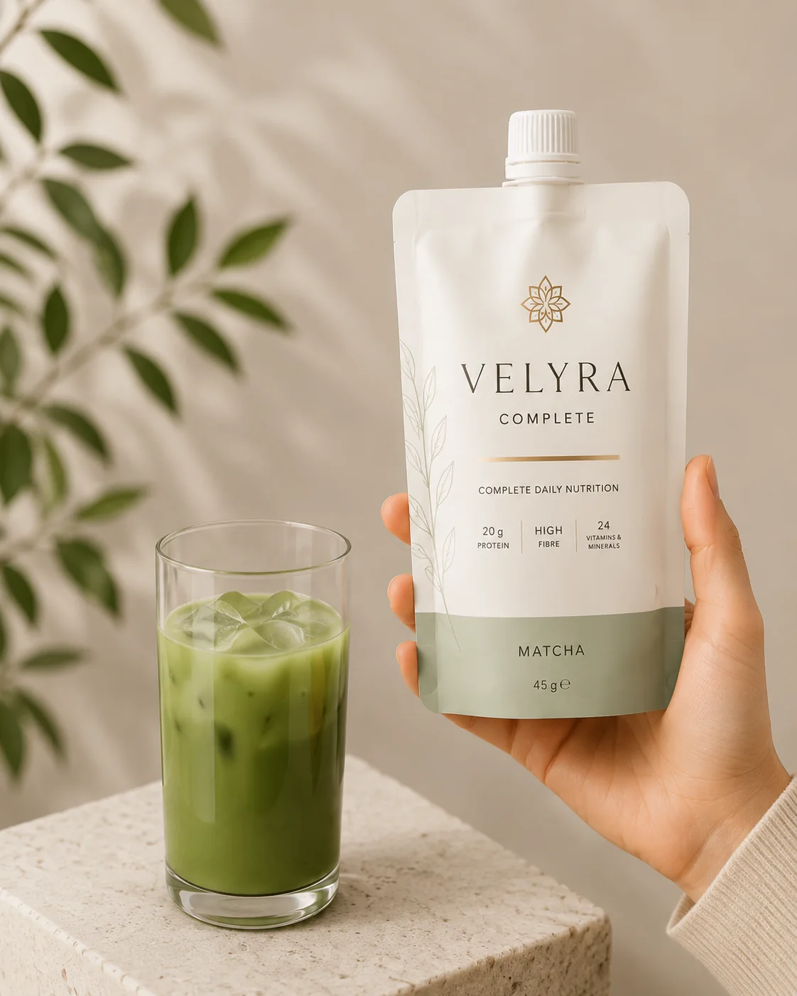 VELYRA COMPLETE Matcha pouch held in hand next to an iced green drink